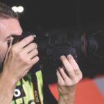 A man in a fluorescent t-shirt holding a professional camera up to his eye