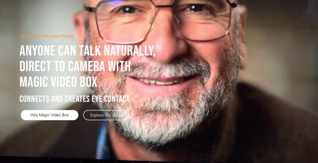 A man with a white beard and glasses smiling and sitting close to the camera with a white caption next to him