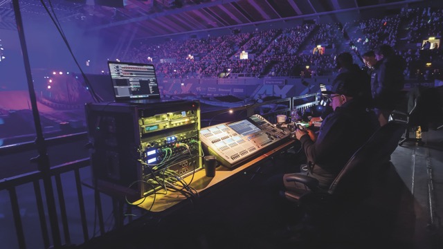 A lighting desk in a purple-lit arena