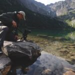 A man working a camera on a cliff edge in a mountainous region