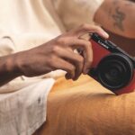A man holding a red Panasonic Lumix S9 camera resting one corner on his yellow shorts