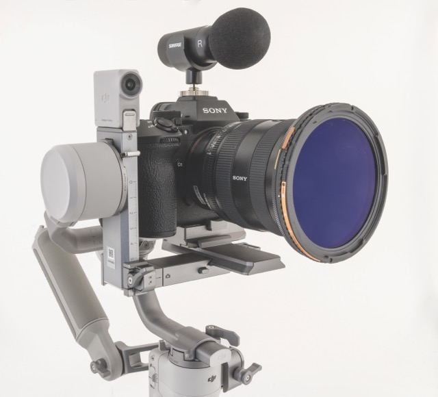 A professional camera with a care lens attached to a grey mount and with a microphone attached to the top