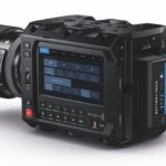 A professional camera with a screen on the side. It faces away against a white background