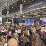 A conference with a crowd sitting and watching a speaker on a stage
