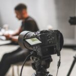 Two cameras on tripods filming a man in the blurred background working at a table