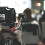 A camera on a stand. A conference takes place in a blurred background