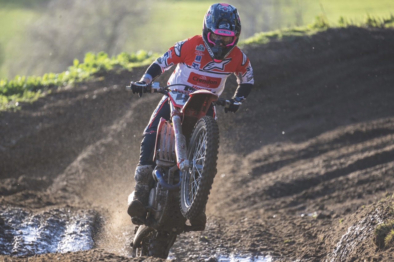 A person wearing a red and white suit and helmet, riding a motorbike over a dirt road
