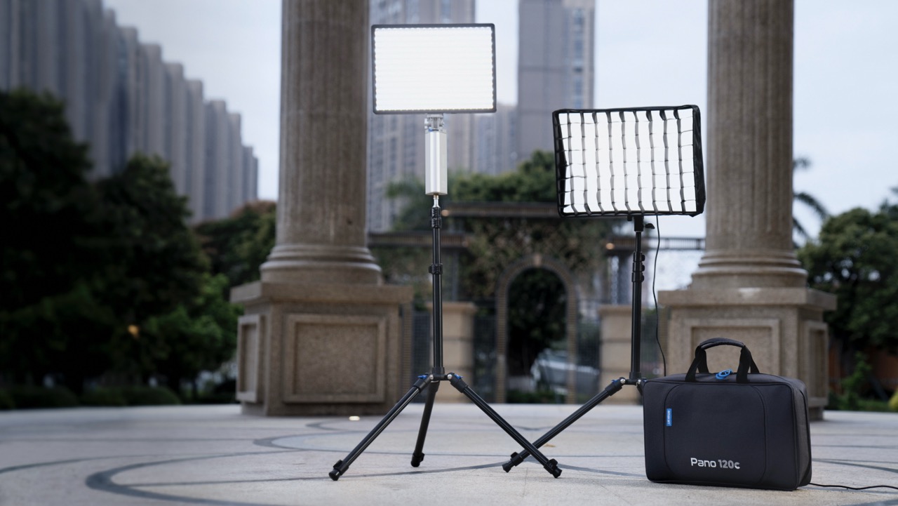 Two LED panels set up outside on a stone floor in front of two large pillars. A black bag is placed on the ground next to them
