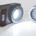 A black device with a bright light circle. A lens sits next to it
