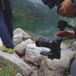The legs of person moving over rocks on a cliff. A person holding a camera on a mount follows