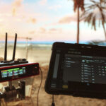 A tablet and a red and black pronged device sitting on a beach landscape