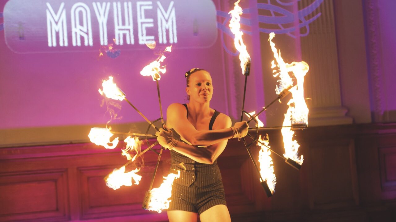 A woman juggling with wheels of fire sticks on a purple stage