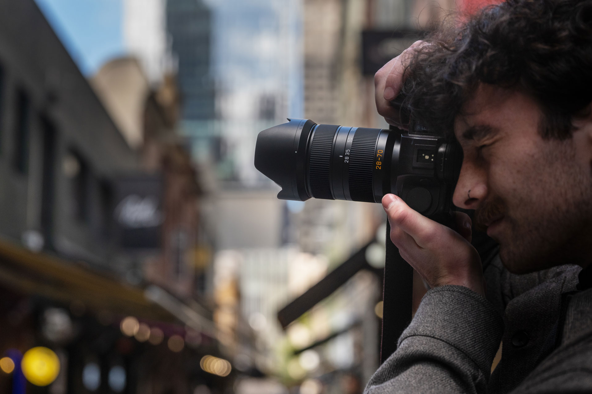 A side view of a man holding a camera with a large lens up to his face in a city landscape