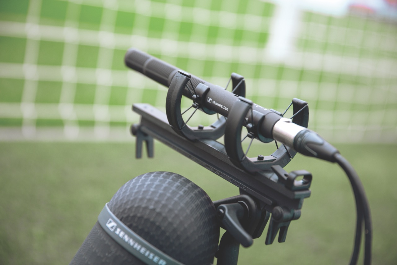 A microphone on a stand. A football pitch and goal are blurred in the background