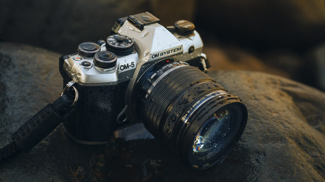 A black and gold camera with a lens attached, sitting on a rock in low lighting