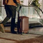 A person walking down the escalator, pulling a brown suitcase along with them