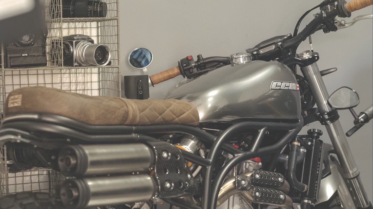 A close-up of a brown and silver motorbike sitting in a garage in front of a shelf with camera gear on