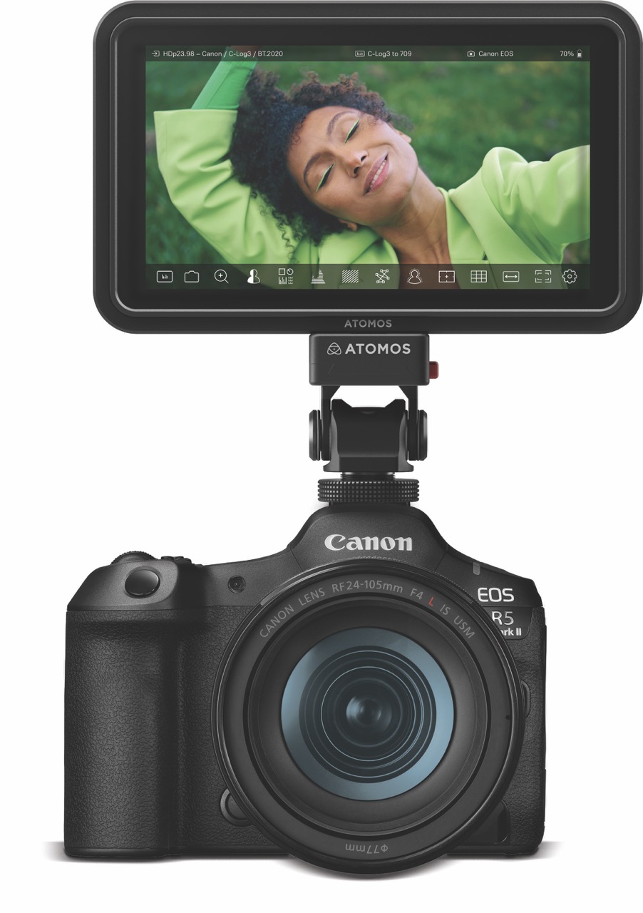 A camera with a monitor attached to the top showing a woman in green smiling and laying on her arm
