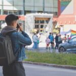 A person standing in the middle of road holding a camera up to their eye as they take a photo of a parade on the opposite side of the street