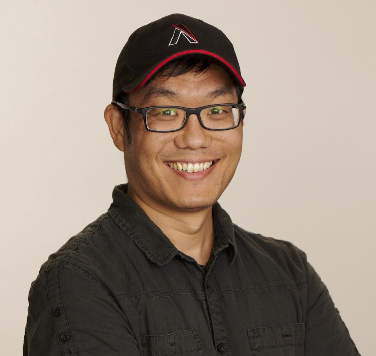 A portrait of a smiling man wearing glasses and a black cap