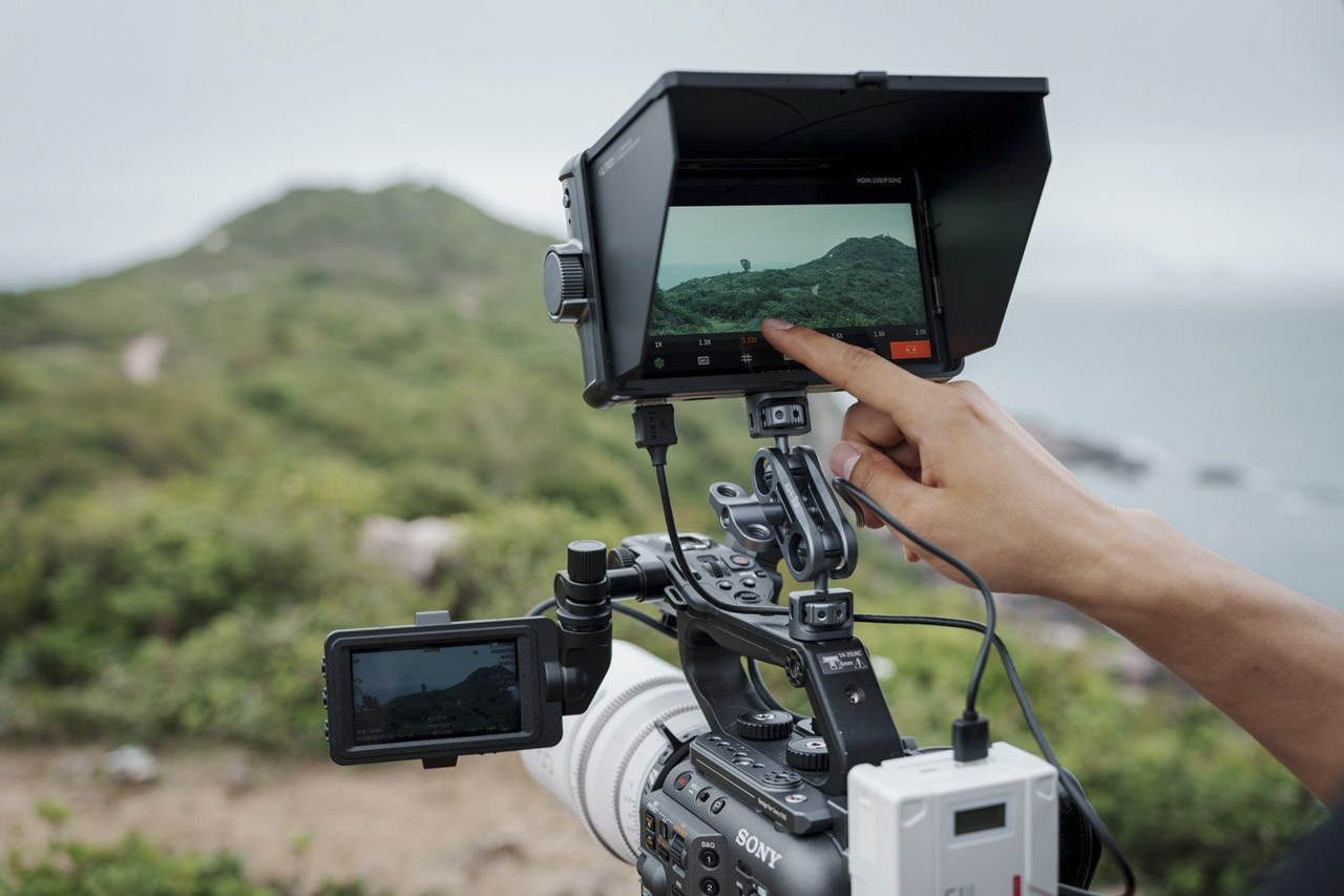 A camera with a monitor attached being used outside on mountain terrain