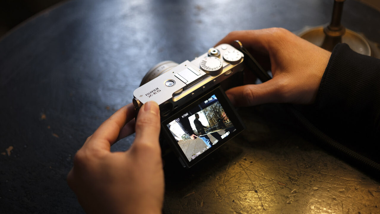A person using a Fujifilm camera with both hands as it rests on a table