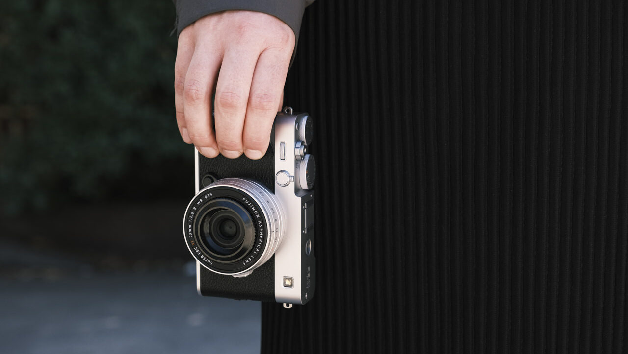 A person wearing black trousers holding a black and silver camera in their fingers
