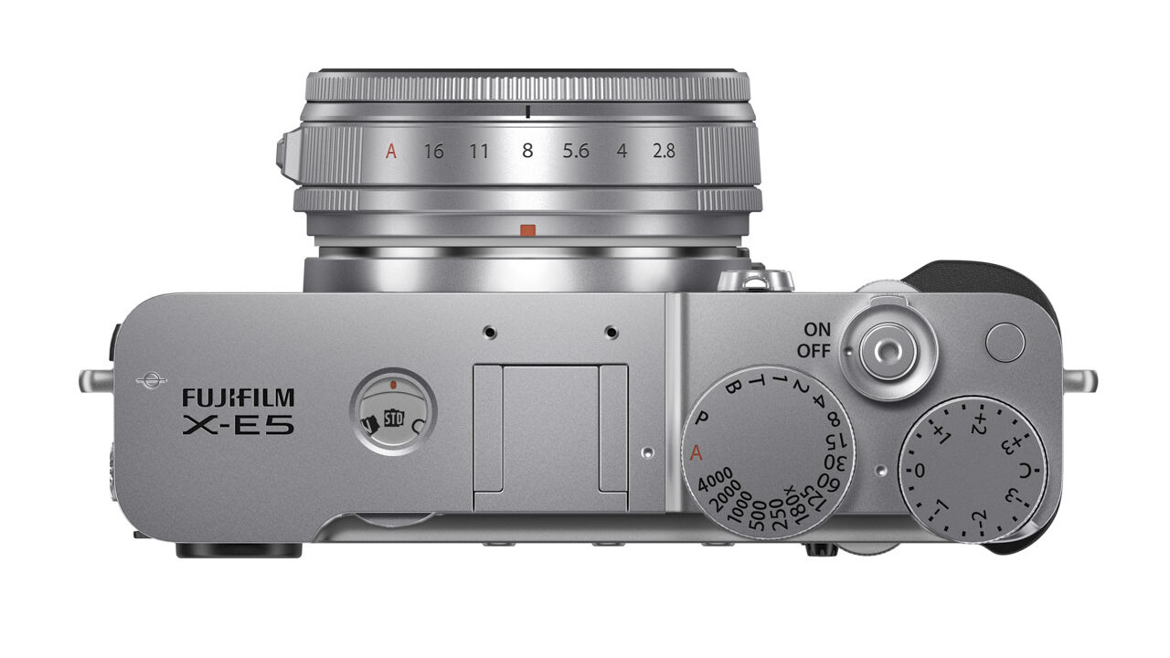 Top view of a silver Fujifilm X-E5 camera with a short lens and three dials in a triangle