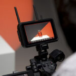 An over-the-shoulder image of an Atomos Ninja TX field monitor showing a product, against an orange background