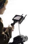 A woman holds an Atomos Ninja TX field monitor, against a white background