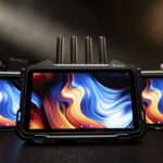 A line of three monitors with blue and orange waves on the screen, against a black background