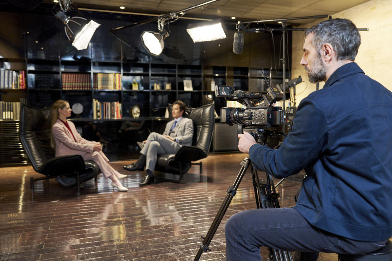 A man operating a Sony Z300 camcorder, filming two people conducting an interview