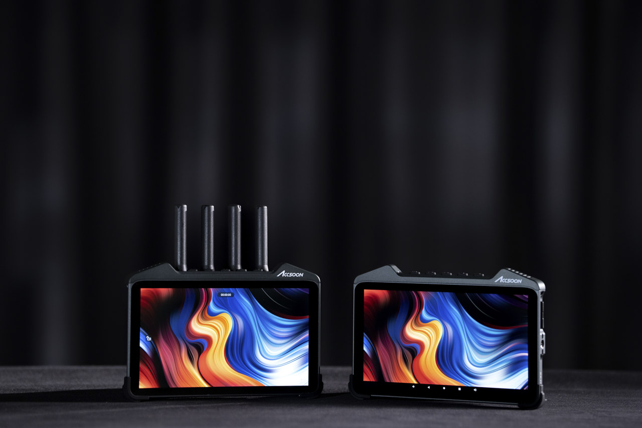 Two monitors sitting side by side with orange and blue waves on the screen, against a black background. The monitor on the left side has four prongs on the top