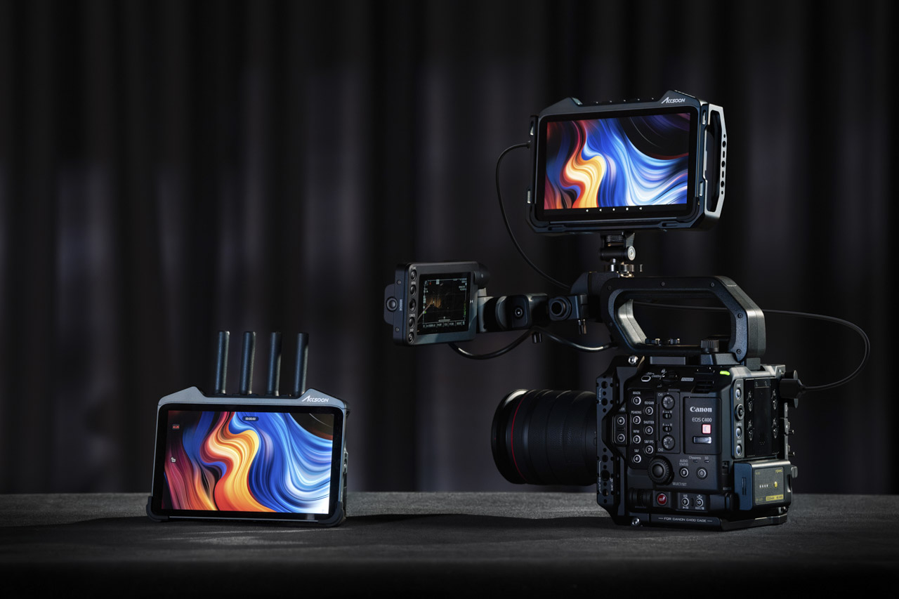 One monitor on a surface next to a camera with another monitor attached to the top, against a black background