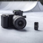 A black camera sits on the floors next to a small black rectangle in a skate park