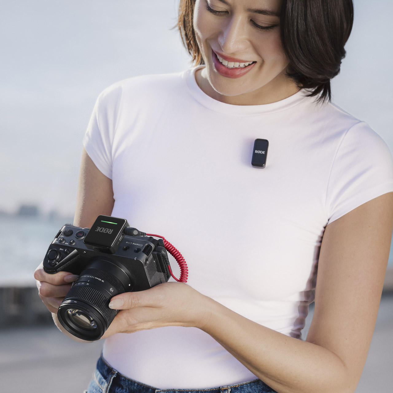 A woman in a white shirt holds a camera with a red cord attached and smiles