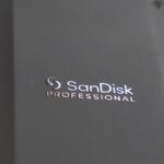 A black storage device from SanDisk with a wire attached, lying on a keyboard