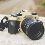 A black and cream camera from OM System sits outside on a stone wall