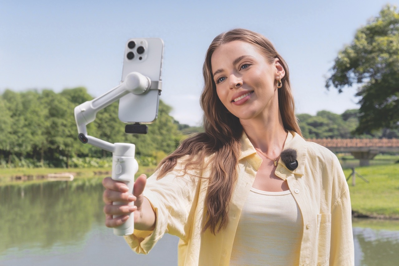 A woman wearing a yellow shirt, holding an iPhone on a white mount. She stands in front of a lake