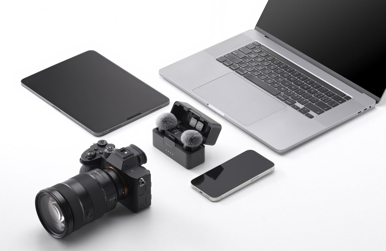 A laptop, tablet, phone and camera, surround a DJI microphone case, against a white background