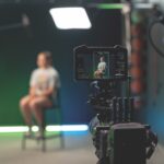 A camera filming a person sitting on a chair in the blurred background