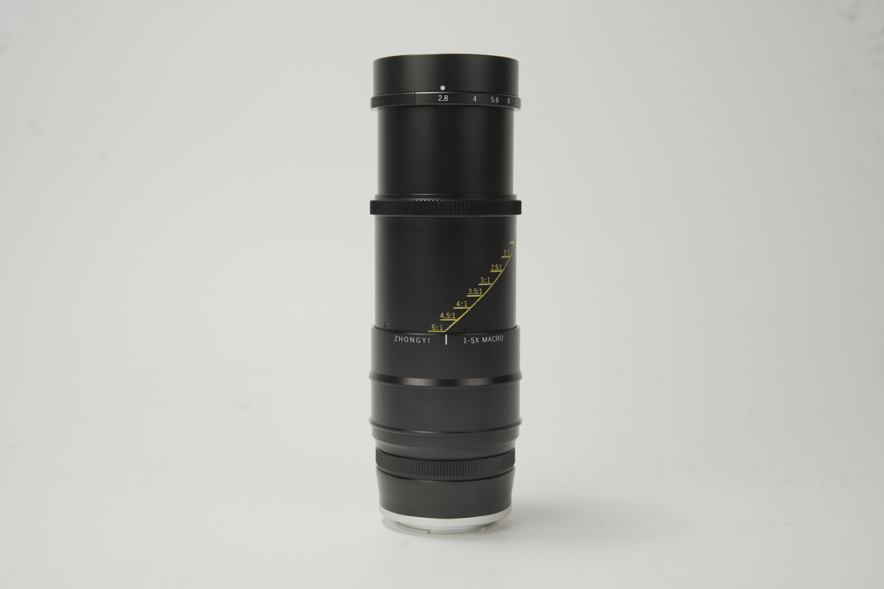 An extended black macro lens from Mitakon sitting on a white surface