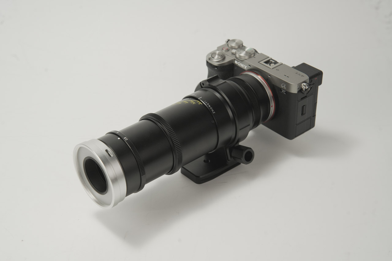 An extended black macro lens from Mitakon with a silver rim, attached to a small camera