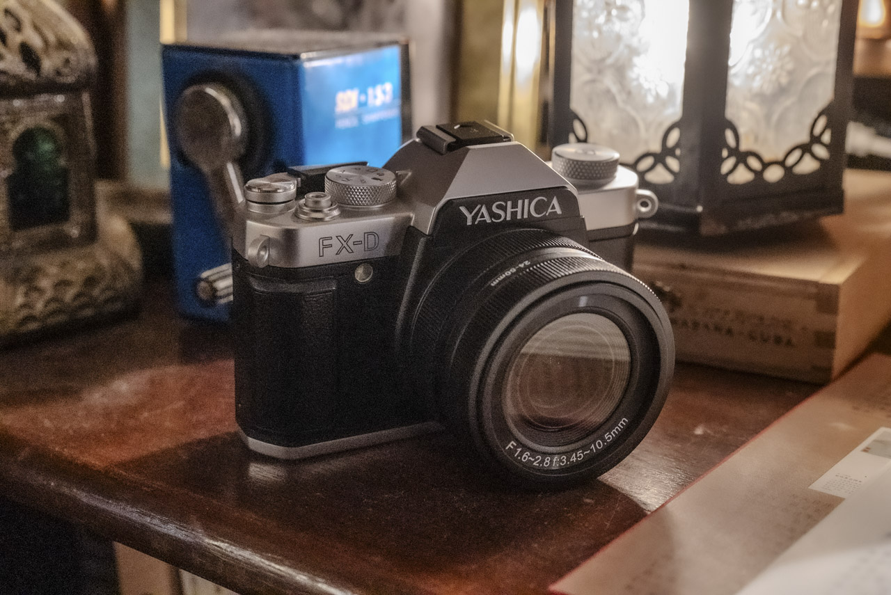 A small Yashica camera sitting on a wooden desk in front of a light and sharpener