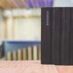 A black portable drive from Samsung sitting on a wooden table with a blurred background