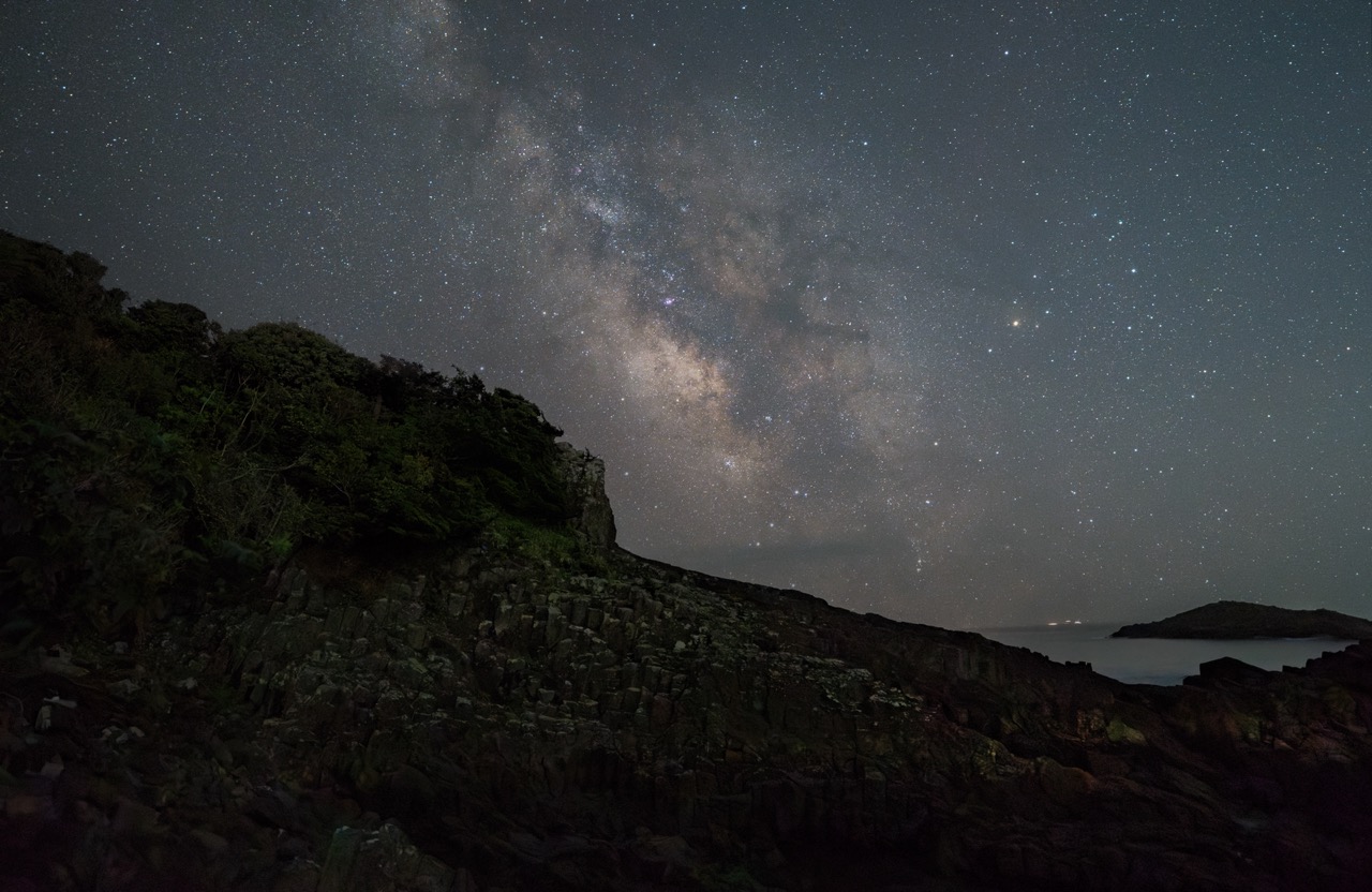 A night sky photo showing the stars behind a silhouetted cliff