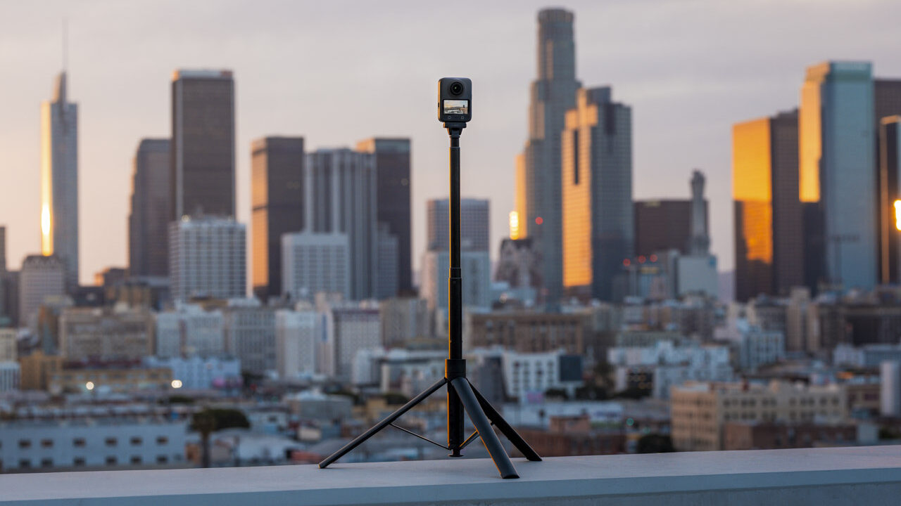 A DJI Osmo 360 on a tripod, sitting on a wall overlooking a cityscape at sunset