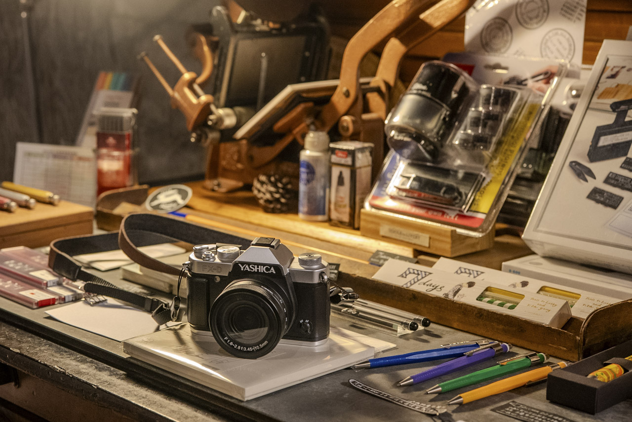 A Yashica camera sits on a desk packed with art supplies