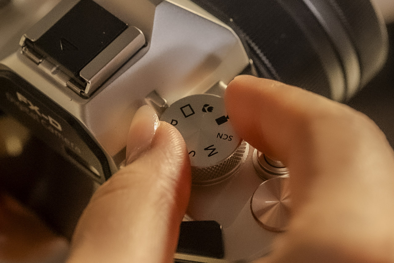 A pair fingers adjusting a dial on the top of a black and silver Yashica camera