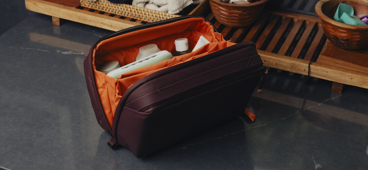 An open black and orange bag from Peak Design with a wooden bench behind